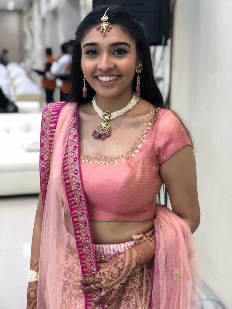 Happy client wearing traditional Indian jewelry including Kai bracelet, choker and earrings with custom maangtikka with a pink lehenga for sister’s wedding ceremony- jewelry styling inspiration