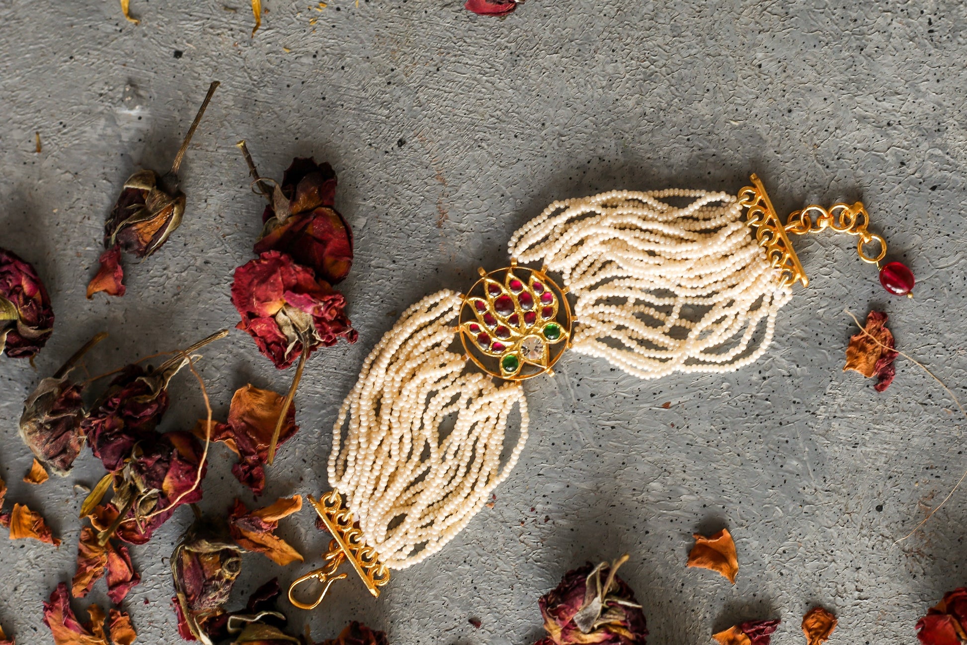 Kai Bracelet close-up view showing detailed lotus design with ox-blood red kemp stones and multiple white pearl strands