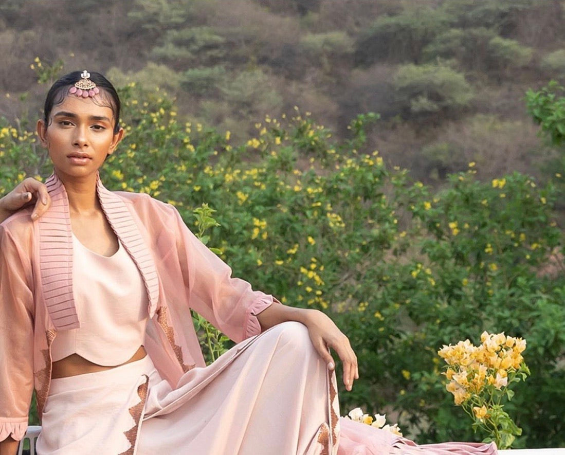 Abharika temple jewelry maang tikka styled for contemporary wear - model in pink ensemble against natural landscape with blooming flowers