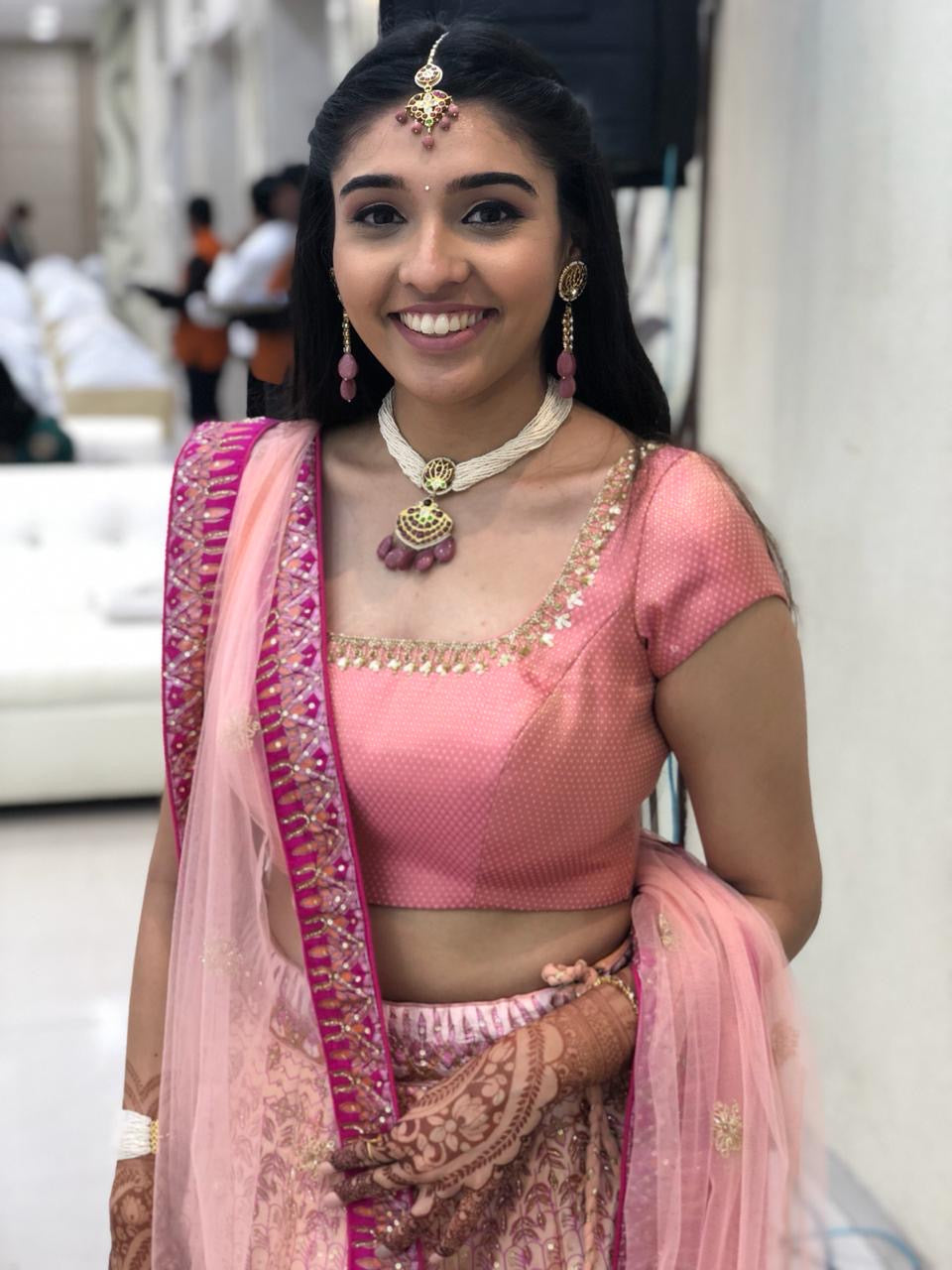 Client wearing traditional Indian jewelry including ornate drop Kai earrings, maang tikka, and choker necklace with pink lehenga for festive styling inspiration