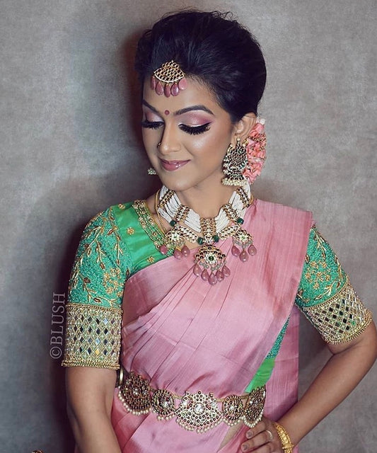 Model wearing complete Abharika temple jewelry set styled by Malaysian makeup artist Blush Beauty Beyond - featuring maang tikka, statement earrings, layered necklaces, and waist belt (Oddiyanam) with pink silk saree and green embroidered blouse for traditional Indian bridal look