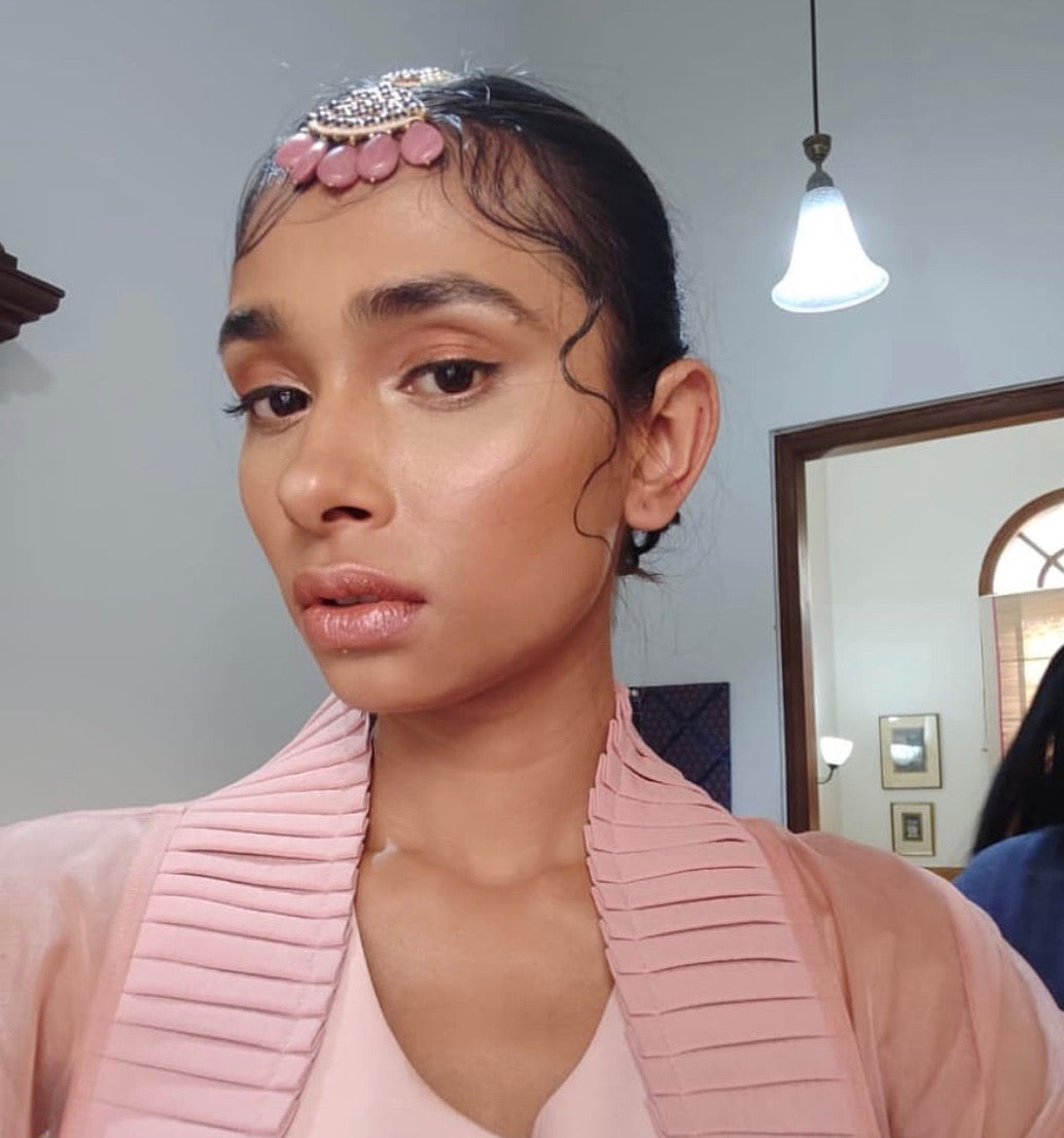 Close-up of model wearing Abharika maang tikka with pink kemp stones and gold detailing, styled with sleek hair and natural makeup in pink coordinated outfit