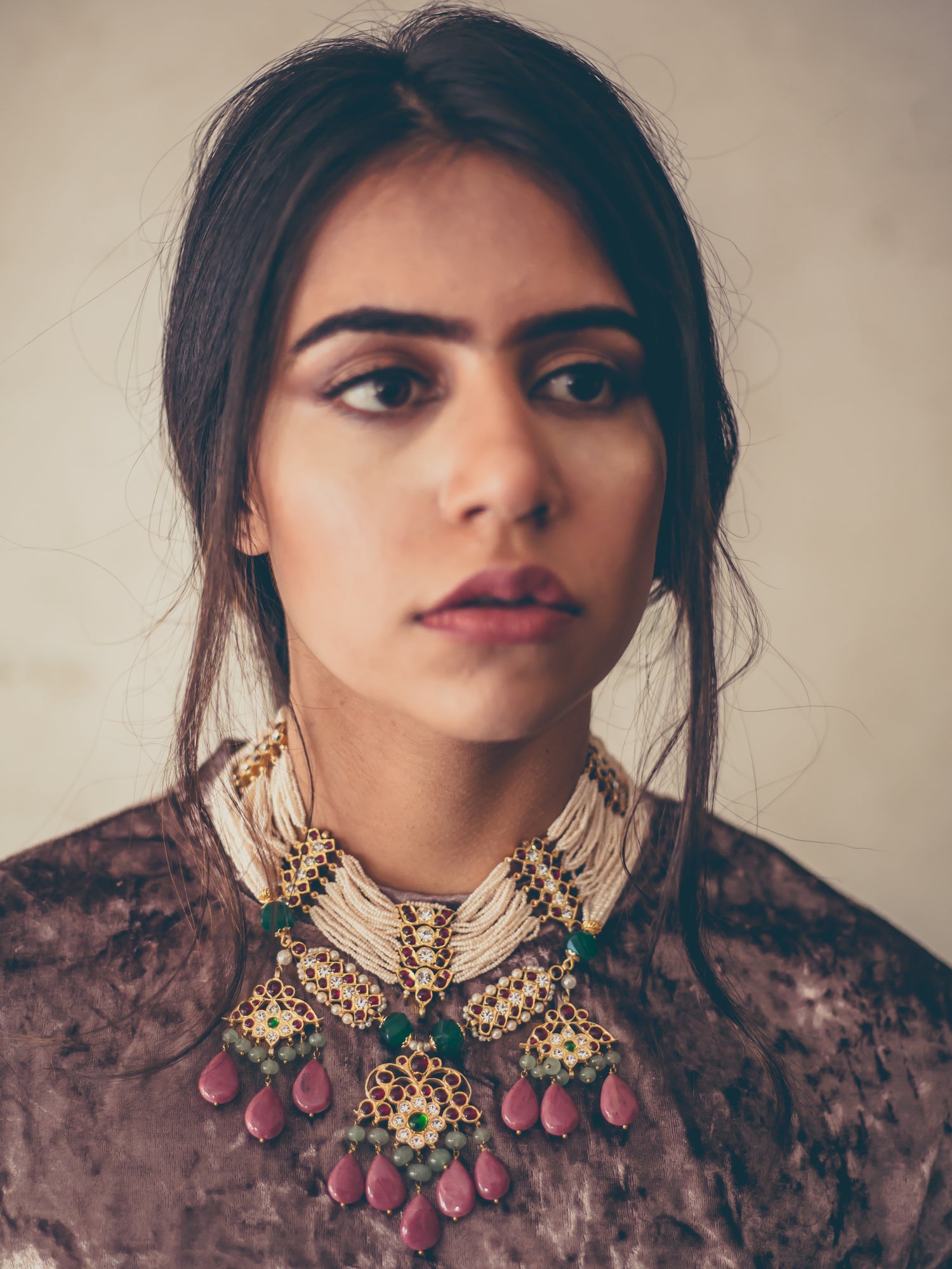 Model wearing the Abharika necklace - ornate sterling silver temple jewelry with red kemp stones and green accents, styled in contemporary style on a pink velvet top