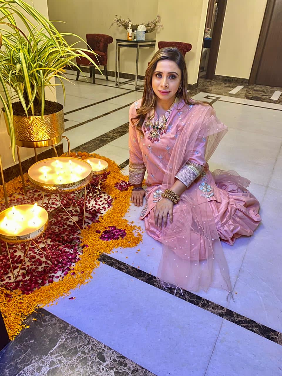 Client wearing Abharika temple necklace in pink ethnic outfit during Diwali celebration with traditional diyas and flower decorations by Aaharya