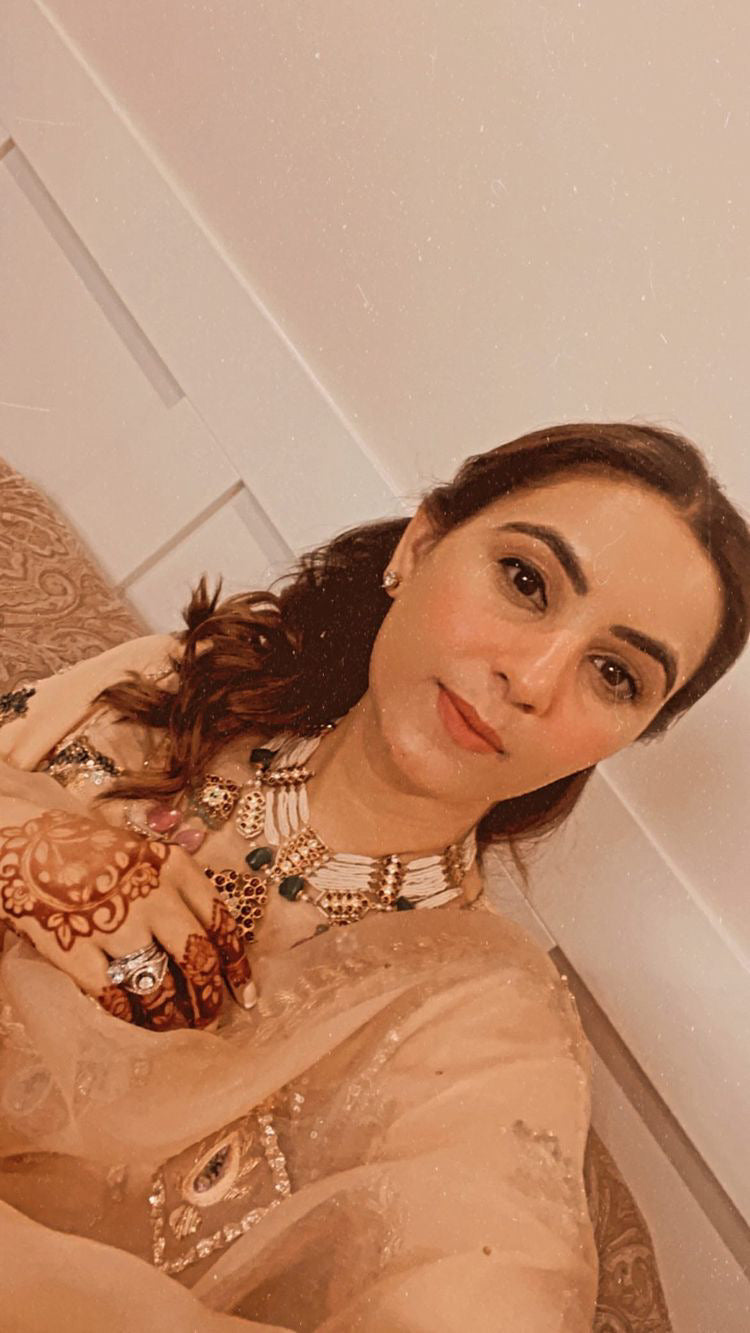 Happy client showcasing Abharika temple necklace with henna-decorated hands in elegant golden outfit by Aaharya